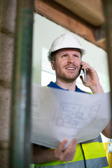 Architect Inside House Being Renovated Studying Plans Talking On Mobile Phone