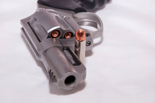 A stainless 357 magnum revolver with a single bullet next to it shown on a white background