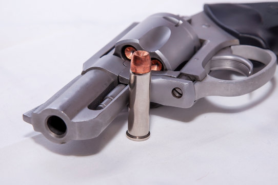 A stainless 357 magnum revolver with a single bullet next to it shown on a white background