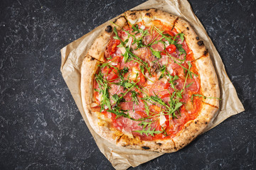 Pizza with prosciutto, arugula and parmesan on black stone background. Top view.