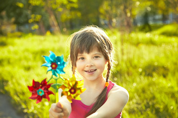 cheerful little girl playing with pinwheel in summer park