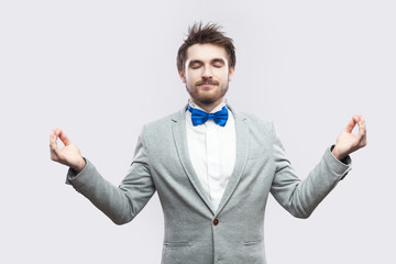 Portrait of calm relax handsome bearded man in casual grey suit and blue bow tie standing with...