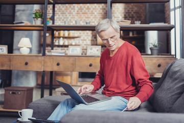 Modern pensioner holding a laptop while sitting on the sofa