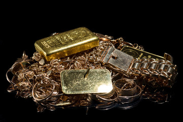 A pile of gold bars and gold jewelry on the black background. Selective focus.