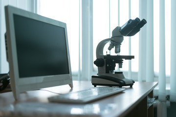 Microscope and a computer on a table in a laboratory on a window light background.