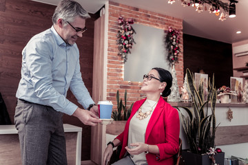 Grey-haired tall man in a blue shirt offering coffee to his colleague