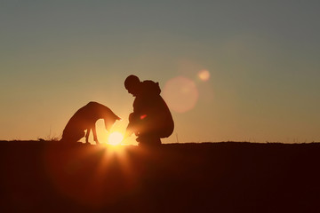 Fototapeta na wymiar The man holds the sun in his hands, the dog is looking at the sun, silhouettes against the sunset