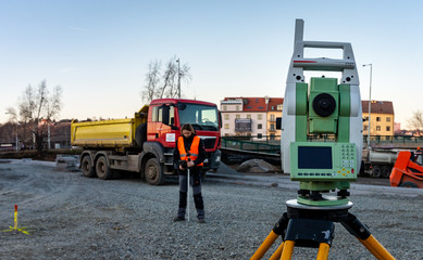 Surveyor engineer with equipment (theodolit or total positioning station) on the construction site of the road with construction machinery background 