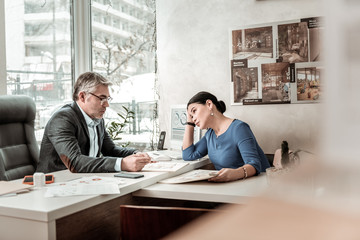 Grey-haired serious man in eyeglasses and his colleague looking serious