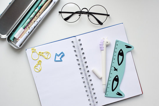 Top View Of An Open Blank Notebook With A Pen In The Form Of A Unicorn, A Pencil Case With Kawaii Pens