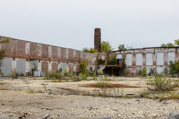 Fototapeta na wymiar Behind the remains of an abandoned factory with tall brick chimney