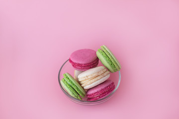 several multi-colored macarons in a glass plate on a pink background