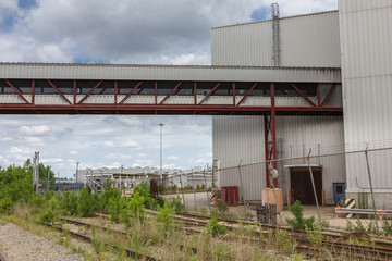 Obraz premium Chodnik nad trawą wypełniony torami kolejowymi do opuszczonej fabryki samochodów