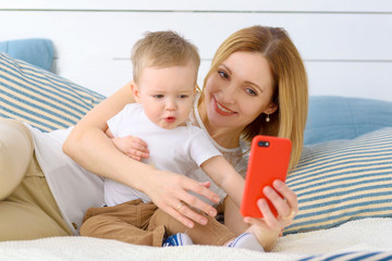 Mother with child baby boy photoshooting on red smartphone selfie in home room