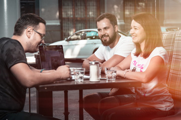Businessmen discuss the deal and control it online, in a cafe on the street. A girl and two guys.