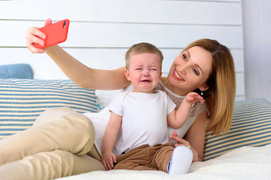 Mother with cry child baby boy photoshooting on red smartphone selfie in home room