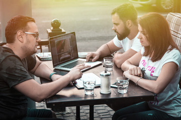 Businessmen discuss the deal and control it online, in a cafe on the street. A girl and two guys.