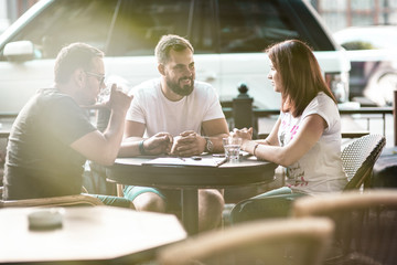 Businessmen discuss the deal and control it online, in a cafe on the street. A girl and two guys.