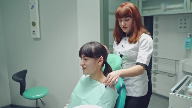 Dentist prepares the smiling patient for teeth treatment on the background of stomatology cabinet. The doctor and young woman in a dentist chair