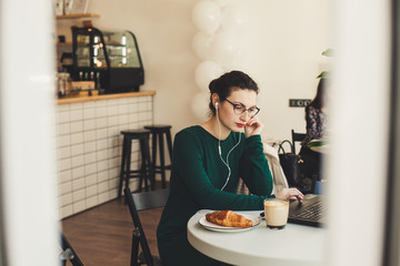 Young modern woman sitting in coffee shop and using notebook