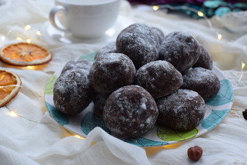 Chocolate gingerbread, sprinkled with powdered sugar on a plate with turquoise leaves, dried orange
