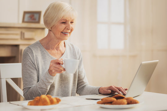 Pensioner smiling while watching family photos on laptop