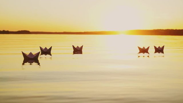 Yellow rays of the evening sun shining on the paper boats swimming in the river at sunset. Origami ships reflects in the water outdoors