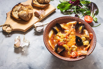 French fish soup Bouillabaisse with seafood, salmon fillet, shrimp, mussels on concrete background.