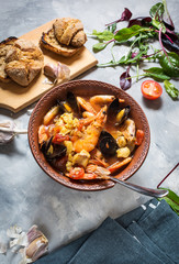 French fish soup Bouillabaisse with seafood, salmon fillet, shrimp, mussels on concrete background.
