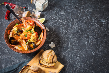 French fish soup Bouillabaisse with seafood, salmon fillet, shrimp, mussels on black stone background. Delicious dinner