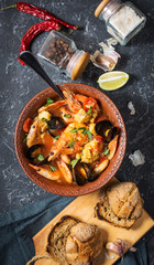 French fish soup Bouillabaisse with seafood, salmon fillet, shrimp, mussels on black stone background. Delicious dinner
