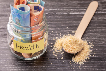 Glass jar with coins and euro banknotes with the inscription HEALTH. A handful of germinated wheat...