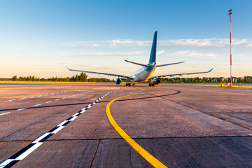 Commercial airplane taxied on the airport platform and is preparing to take off. Taxiways and a plane at sunset. Travel by aircraft concept