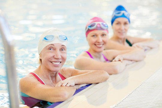 Portrait Of Three Mature Women In Swimming Pool, Leaning On Border And Looking At Camera, Copy Space