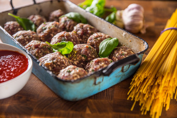 Raw feef meat balls basil tomato sauce garlic and spaghetti on butcher board