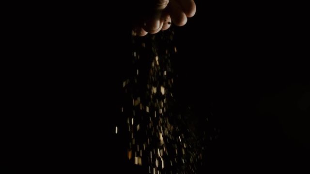 Slow motion shot of pouring spice from the hand against black background