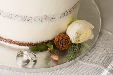 Closeup picture about a detail of white wedding cake with ornaments, with white gold wedding bands