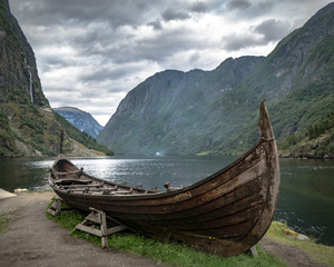 Traditional viking boat near fjord and mountains with dramatic cloudy sky. 