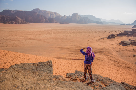 travel and discovery amazing concept photography of lonely girl sight with hand near face stay back to camera on edge of high rock with beautiful picturesque Middle East desert view 