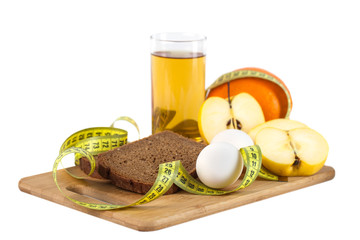 Breakfast including bread, eggs, orange, apple juice on the wooden board with measurement isolated on white