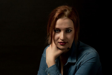 Low key portrait of pensive young woman looking at the camera on the black background. 