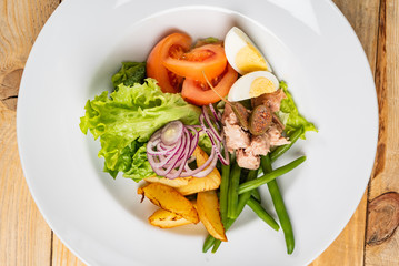 tuna salad, with tomatoes, eggs, red onion and green beans. Wooden background