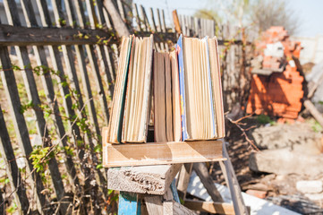 Stack of old books in front of a wooden fence in nature