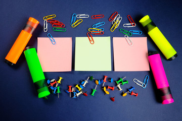 colored paper clips, button, markers and stickers   on a dark blue background. 