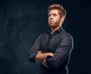 Handsome elegantly dressed redhead man posing with his arms crossed in studio against a dark textured wall