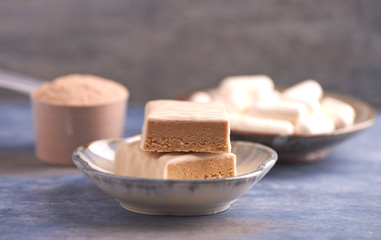 Protein bar in two pieces, creatine capsules and scoop. Bodybuilding food supplements on rustic wooden background. Copy space.