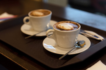 two cups of coffee with milk or latte or cappuccino on the metallic tray on the wooden table outdoor.