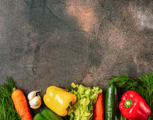 Dark rustic background with a border of fresh vegetables. Top view.