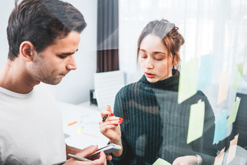 Concentrated coworking team post it notes sticky on glass wall while working and business meeting in office studio. Group creative manager brainstorming work project