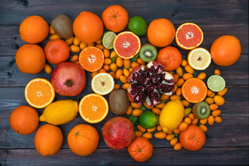 Fruit mixed oranges, tangerines, lemons, lime, kiwi and pomegranate lie on a black wooden background from boards.